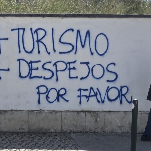 Graffiti on a wall in Graça, Lisbon saying “+ turismo + despejos”, meaning more tourism, more evictions.
