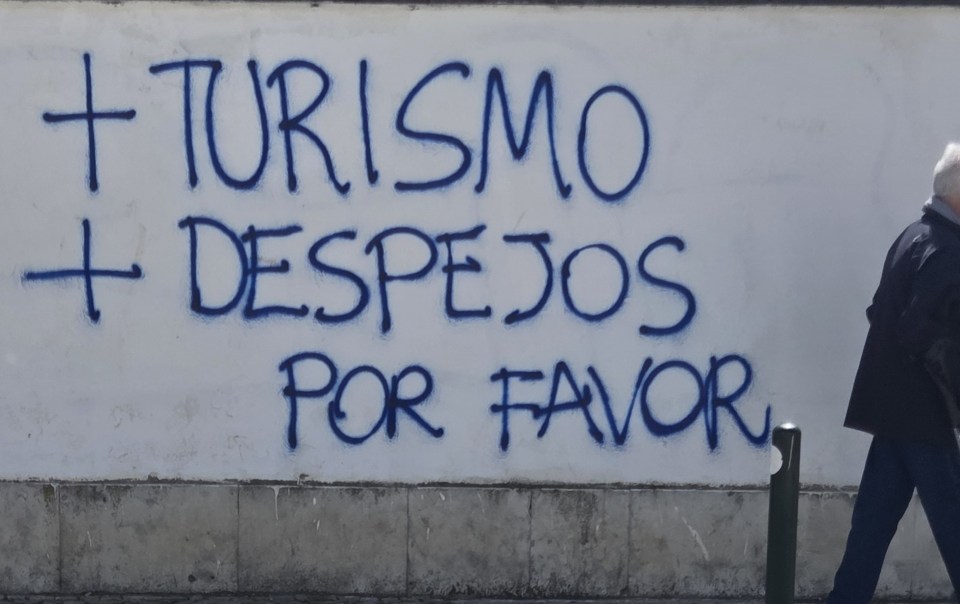 Graffiti on a wall in Graça, Lisbon saying “+ turismo + despejos”, meaning more tourism, more evictions.