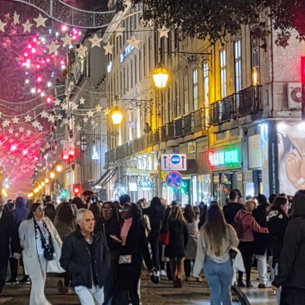 Massive street crowds walking under glowing star canopy christmas lights in lisbon at night.