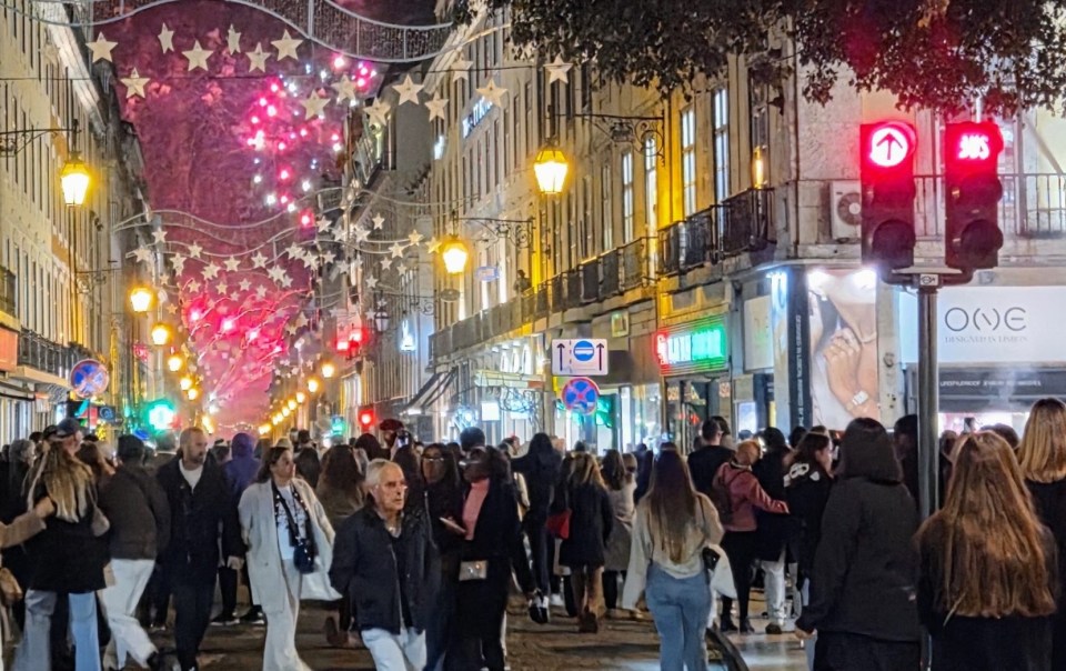 Massive street crowds walking under glowing star canopy christmas lights in lisbon at night.